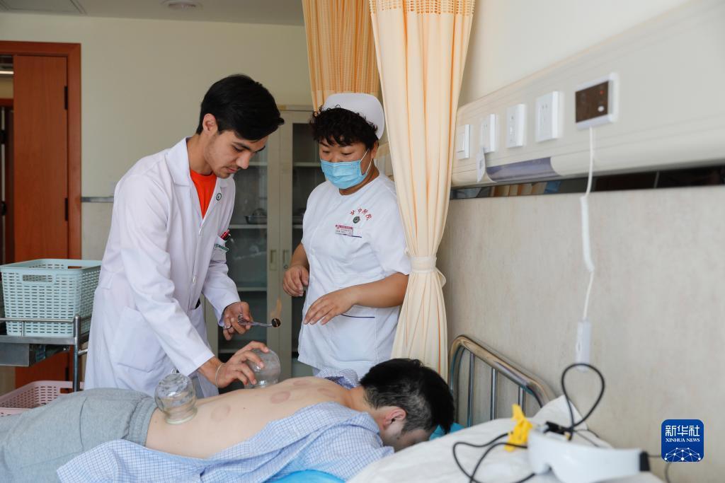 甘肃中医药大学针灸推拿专业的土库曼斯坦留学生迪达（左）在甘肃中医药大学附属医院护士的指导下为患者进行拔罐治疗（7月28日摄）。新华社记者 方欣 摄