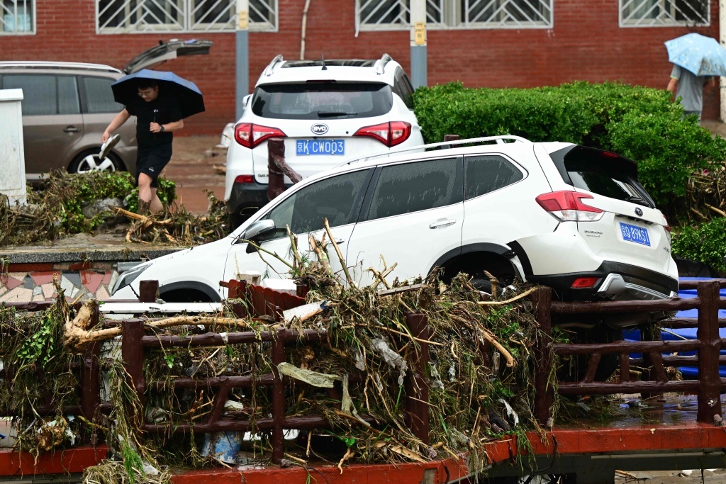 7月31日，北京门头沟，一名男子路过一辆受损抛锚的汽车。洪水退去后，道路上残留不少树枝。