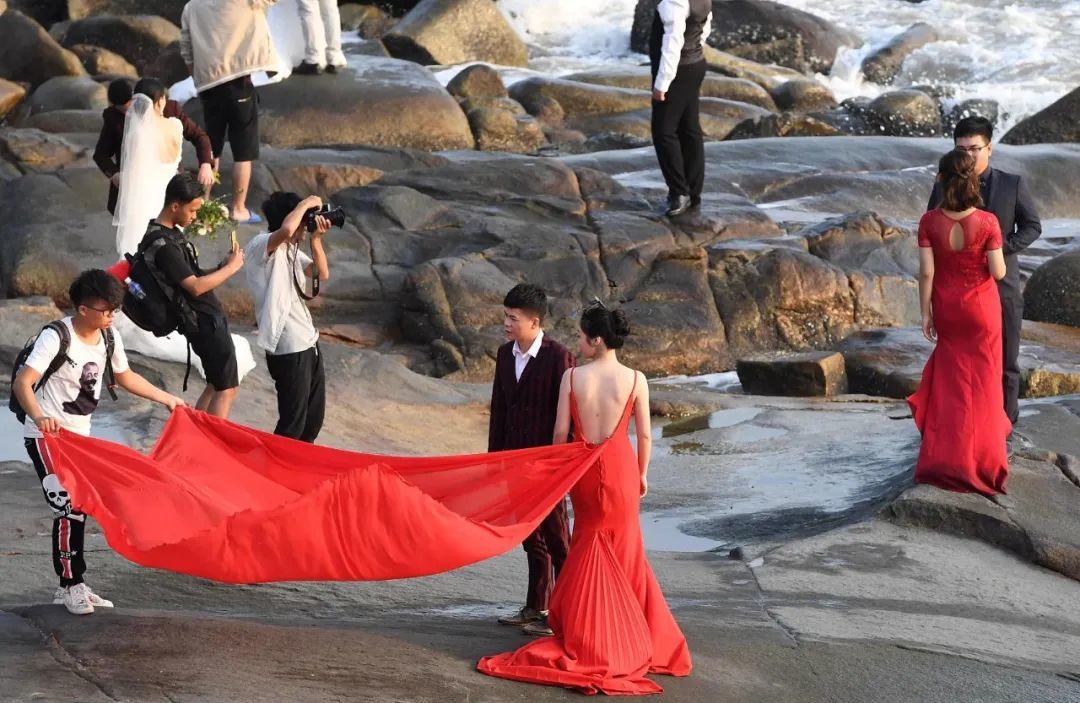 在福建厦门环岛路上一处海滩礁石上，新人扎堆拍摄婚纱照/图源：视觉中国