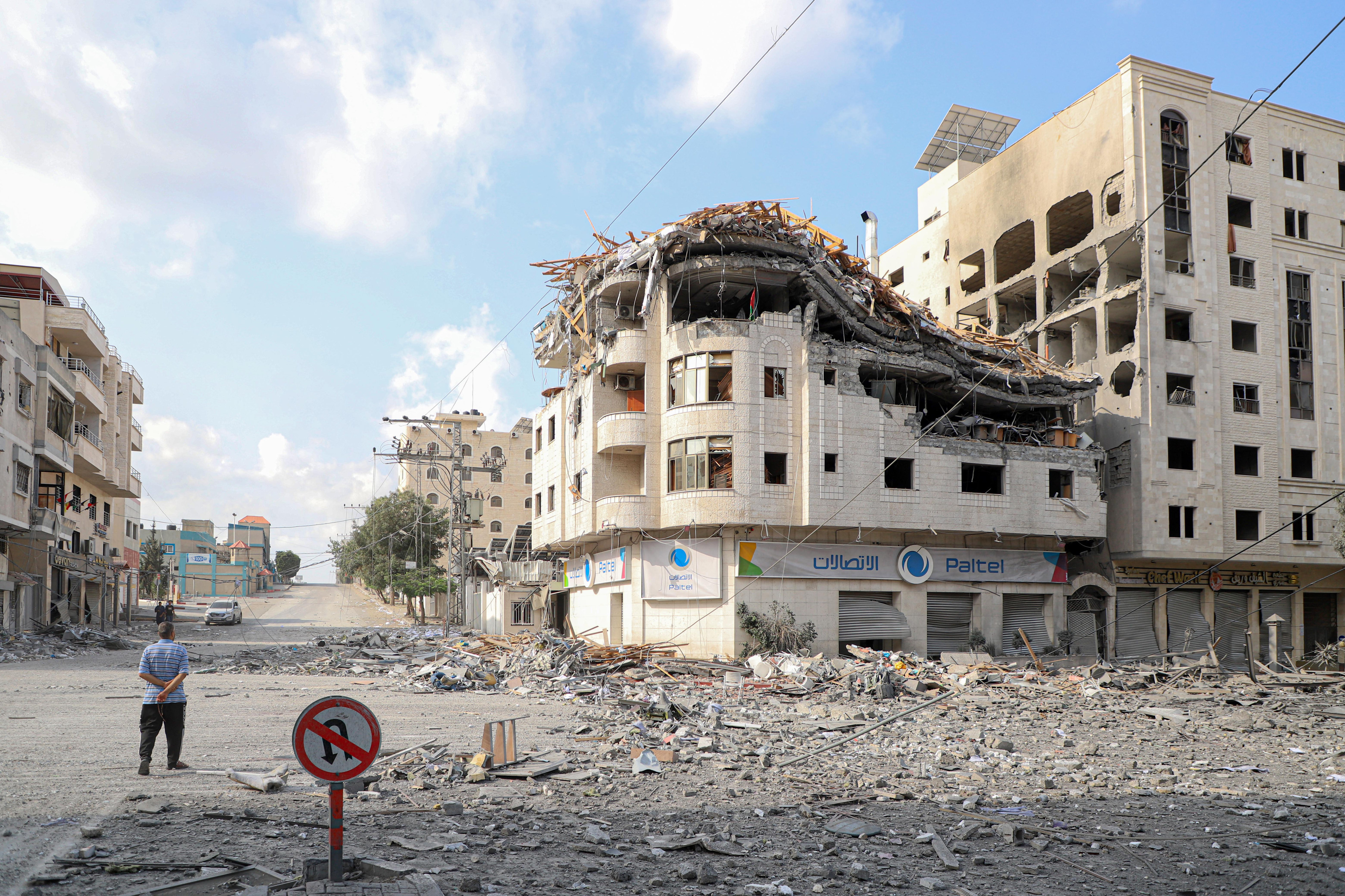 10月10日，在加沙城，人们走过被以色列空袭炸毁的建筑废墟。新华社发（里泽克·阿卜杜勒贾瓦德摄）