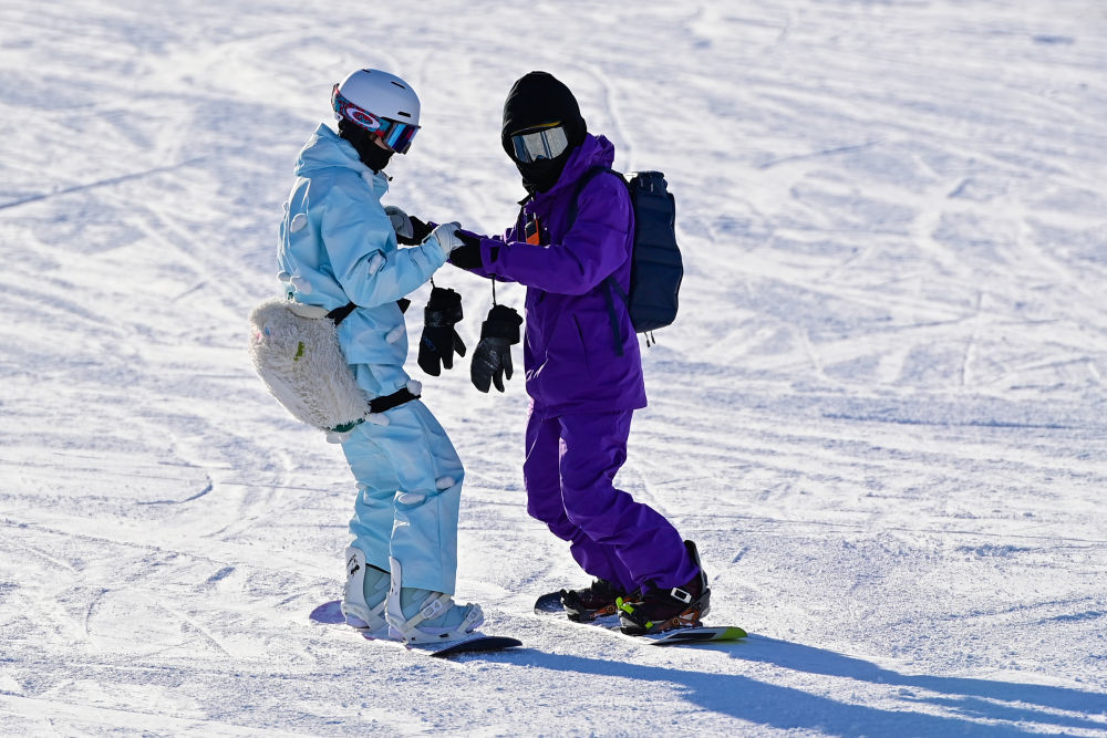 ↑在新疆阿勒泰将军山国际滑雪度假区，一名滑雪爱好者在同伴的帮助下练习滑雪（12月19日摄）。