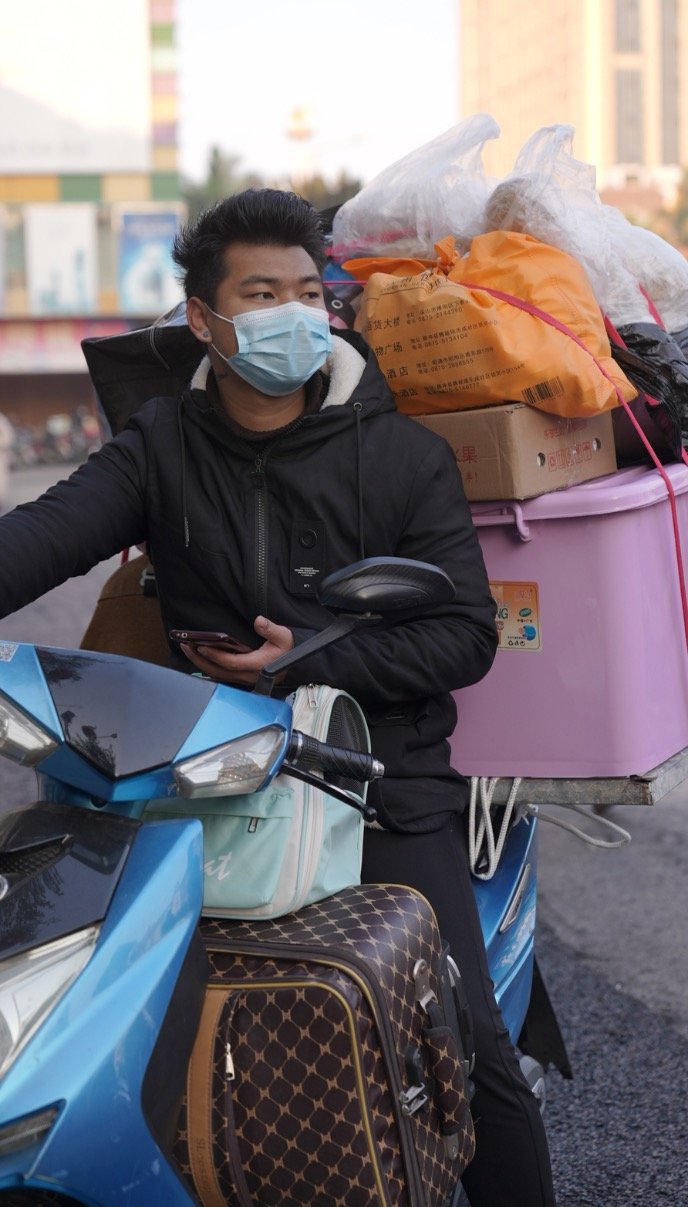 1月8日,缅甸小伙奥奈威(音)骑着电动车带着行李,行李箱装着他的狗,等待从瑞丽口岸出关回到缅甸。。