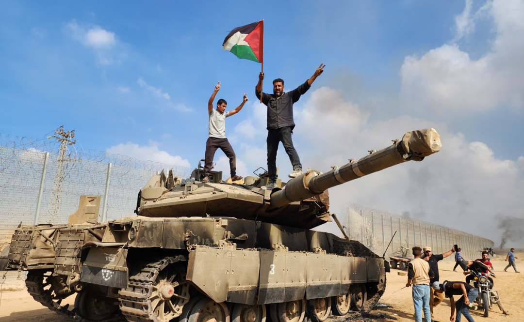 10月7日，巴勒斯坦人在被击毁的以色列坦克上举着巴勒斯坦国旗摆姿势（图源：路透社）