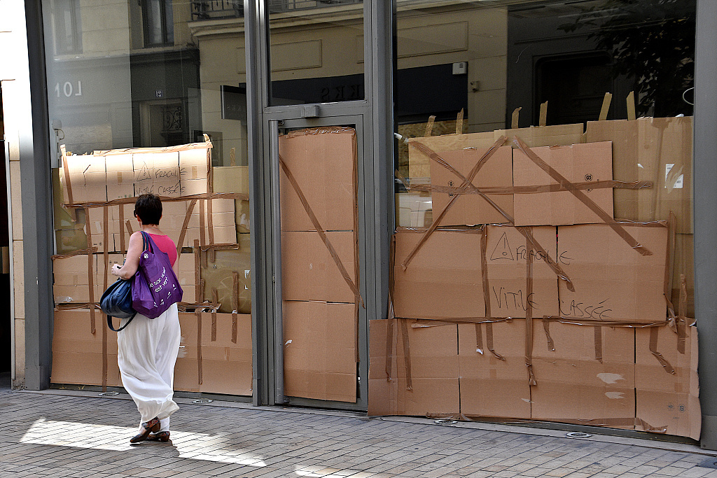 当地时间2023年7月3日，法国马赛，一位行人走过一家商店的外立面，商店损坏的窗户被保护纸板保护着。 视觉中国 图