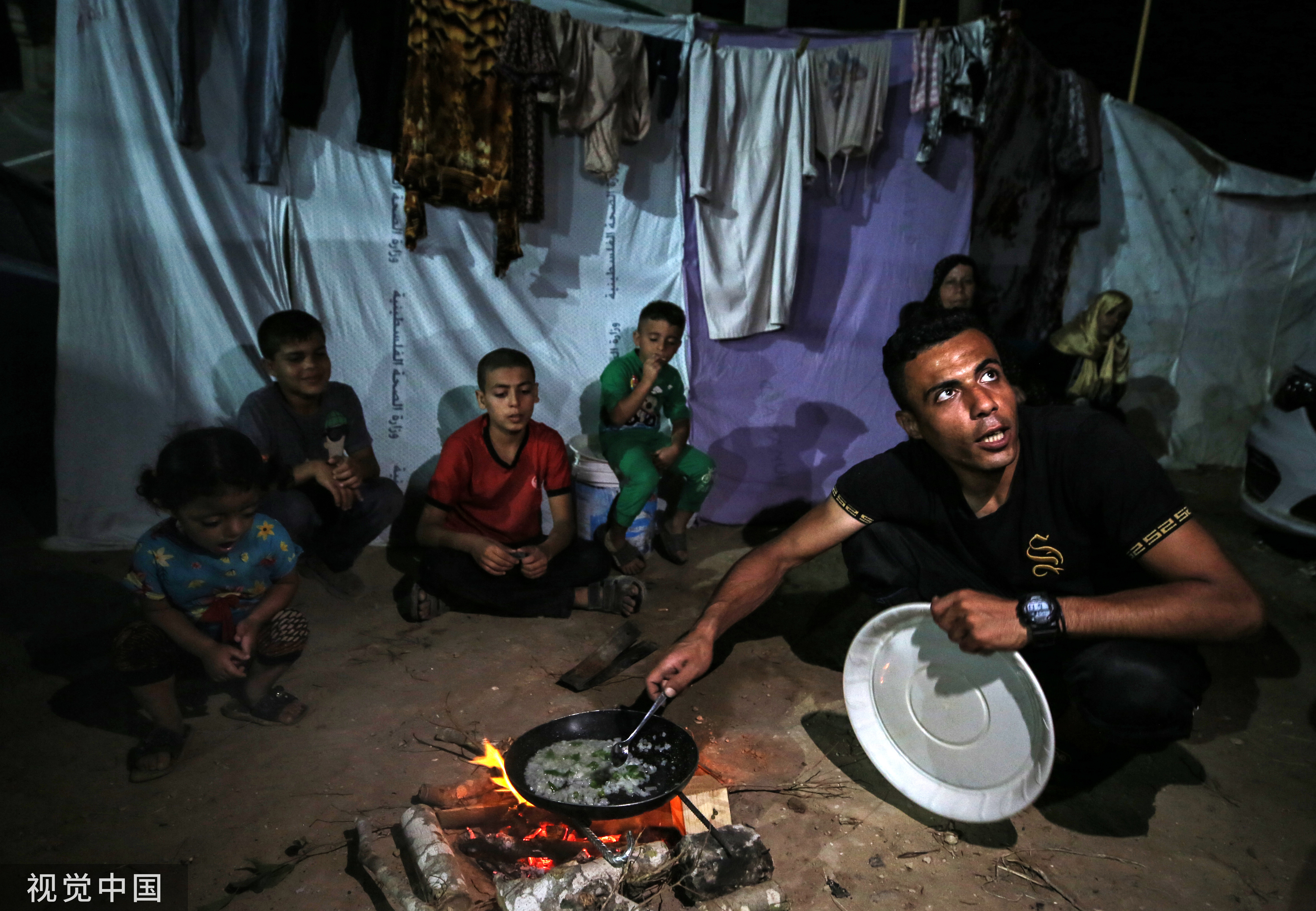 当地时间11月13日，加沙地带代尔拜拉赫，巴以冲突持续，流离失所的巴勒斯坦人在Shuhada Al-Aqsa医院的营地里准备食物。（图：视觉中国）