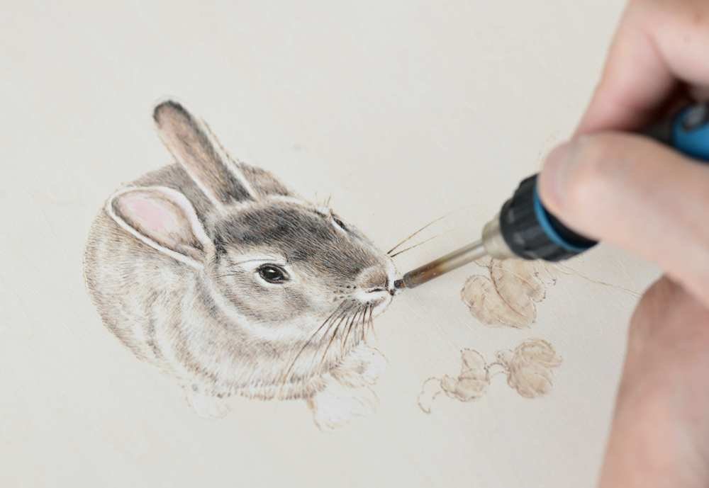 ↑1月20日，在石家莊市新華區灣里廟步行街，烙畫藝人在創作兔子主題的烙畫作品。新華社發（陳其保 攝）