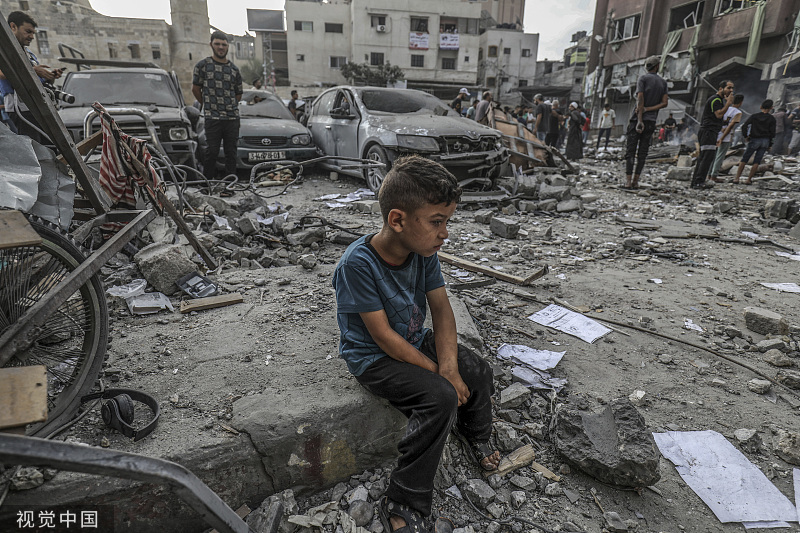 当地时间2023年10月10日，巴勒斯坦加沙地带汗尤尼斯，以色列发动空袭后，一名巴勒斯坦男孩坐在一栋被毁建筑的废墟中。