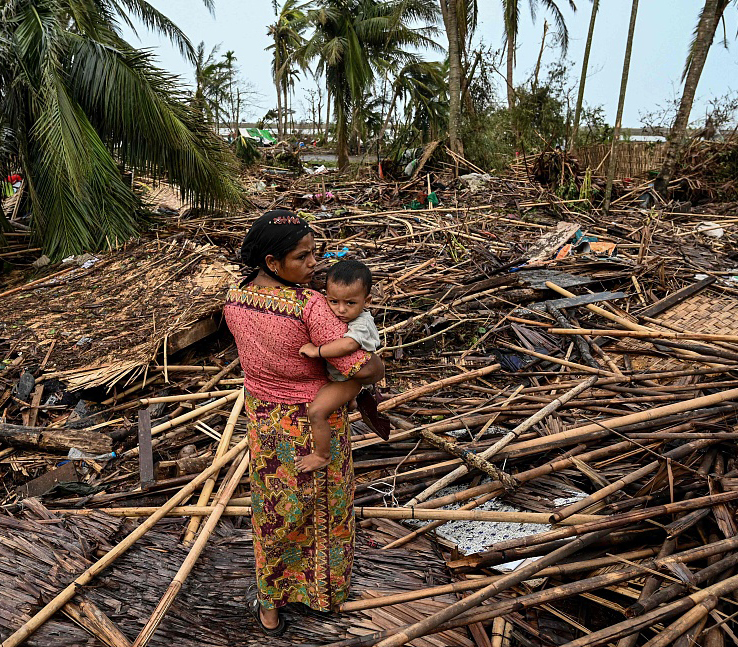 当地时间2023年5月16日，热带气旋“穆查”袭击缅甸实兑，一名罗兴亚妇女抱着她的孩子站在被摧毁的房子旁边。