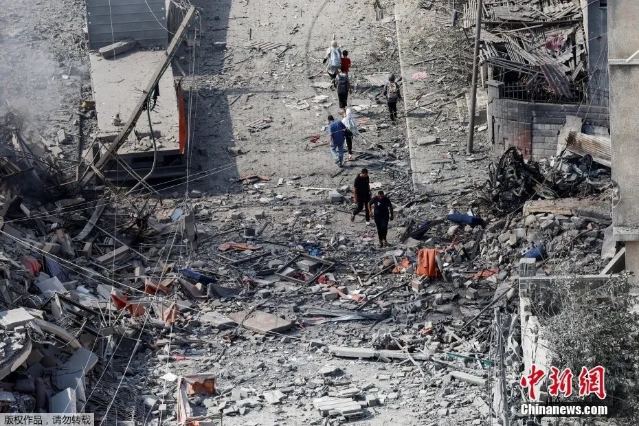 图为当地时间10月10日，加沙地带民众在楼宇废墟中行走。