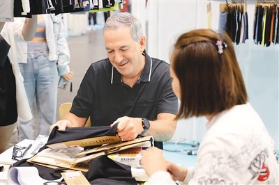 7月19日，在美国纽约举办的第24届中国纺织品服装贸易展览会上，客商（左）在一家中国上海的企业展位选看面料。新华社记者 谢 锷摄