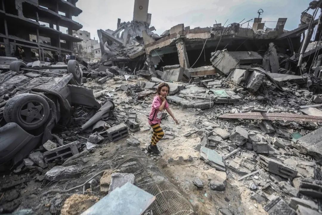 当地时间2023年10月9日，加沙城，以色列空袭Shati难民营后，一名巴勒斯坦女孩走在被毁建筑的废墟上。（视觉中国 供图）