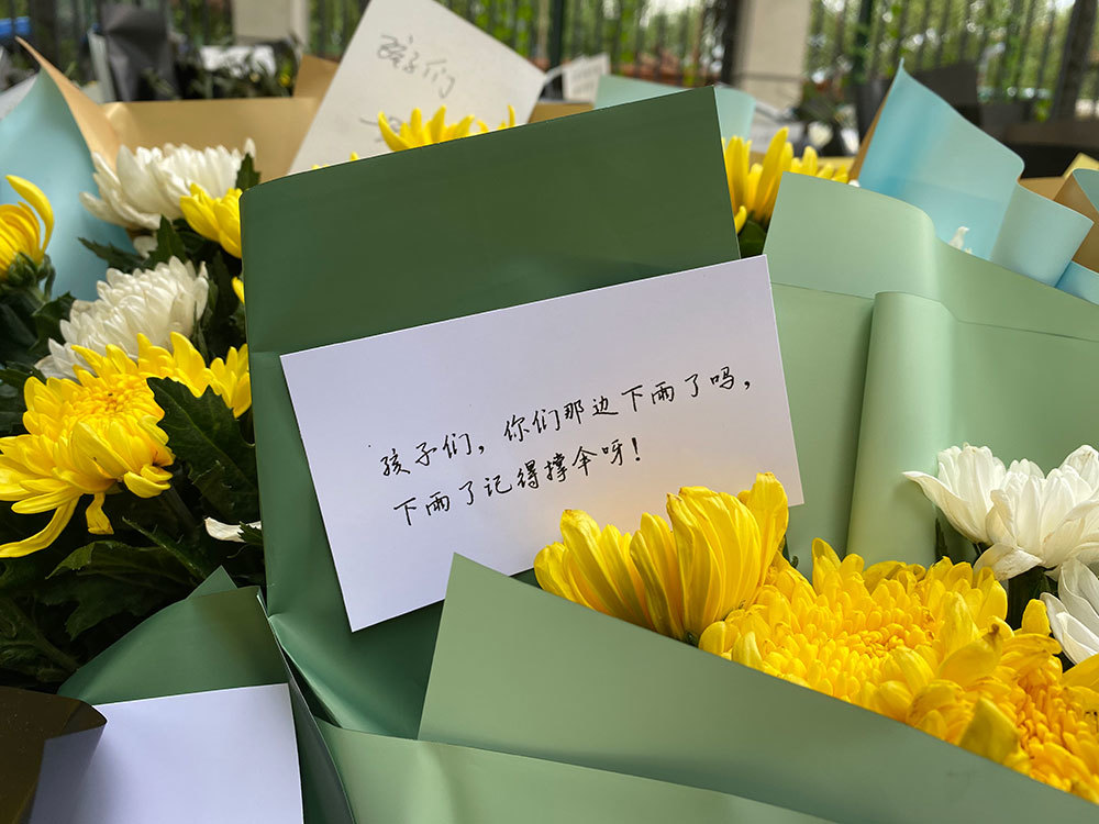 三十四中校门口一束悼念的黄菊，寄语写着：孩子们，你们那边下雨了吗，下雨了记得撑伞。