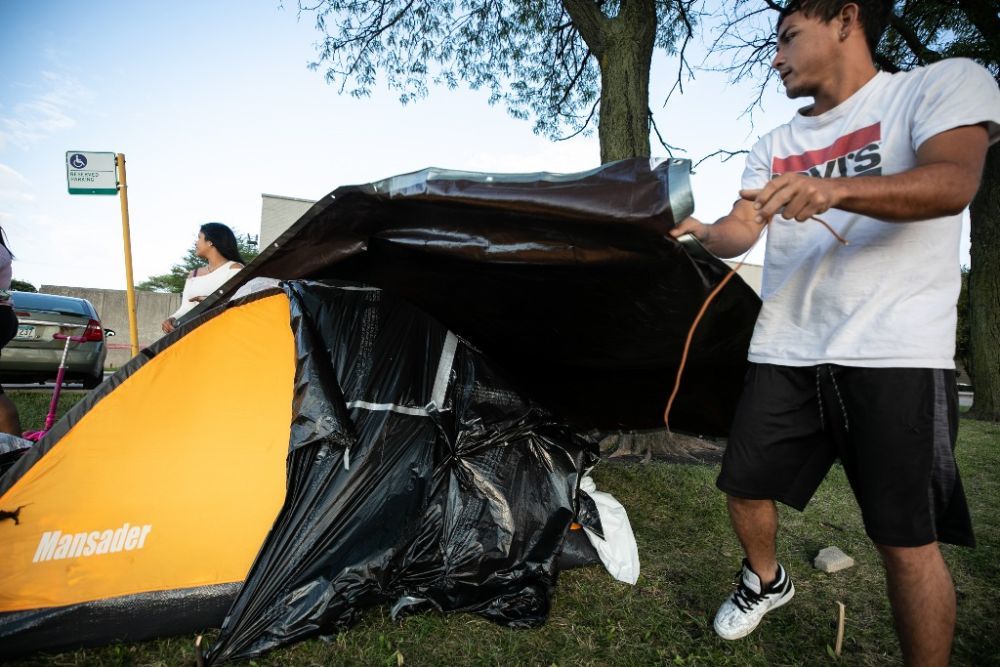 8月17日，在美国伊利诺伊州芝加哥第2区警察局外，一对移民情侣给帐篷盖上防水布。新华社发（文森特·约翰逊摄）