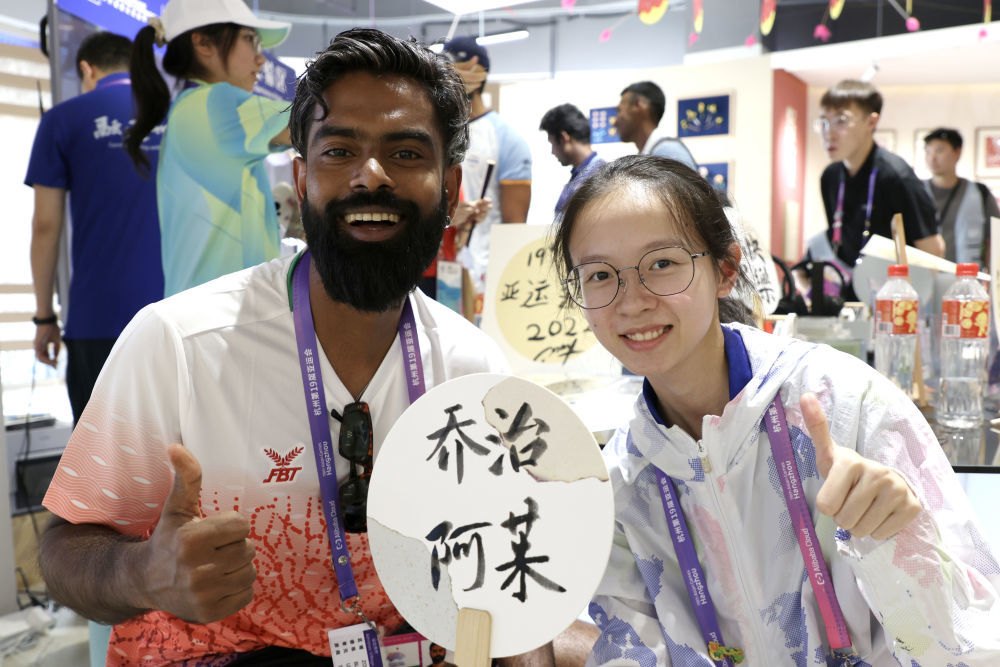 9月29日，马尔代夫羽毛球运动员穆罕默德·阿杰凡·拉希德（左）在亚运村乐活集市与工作人员合影留念。