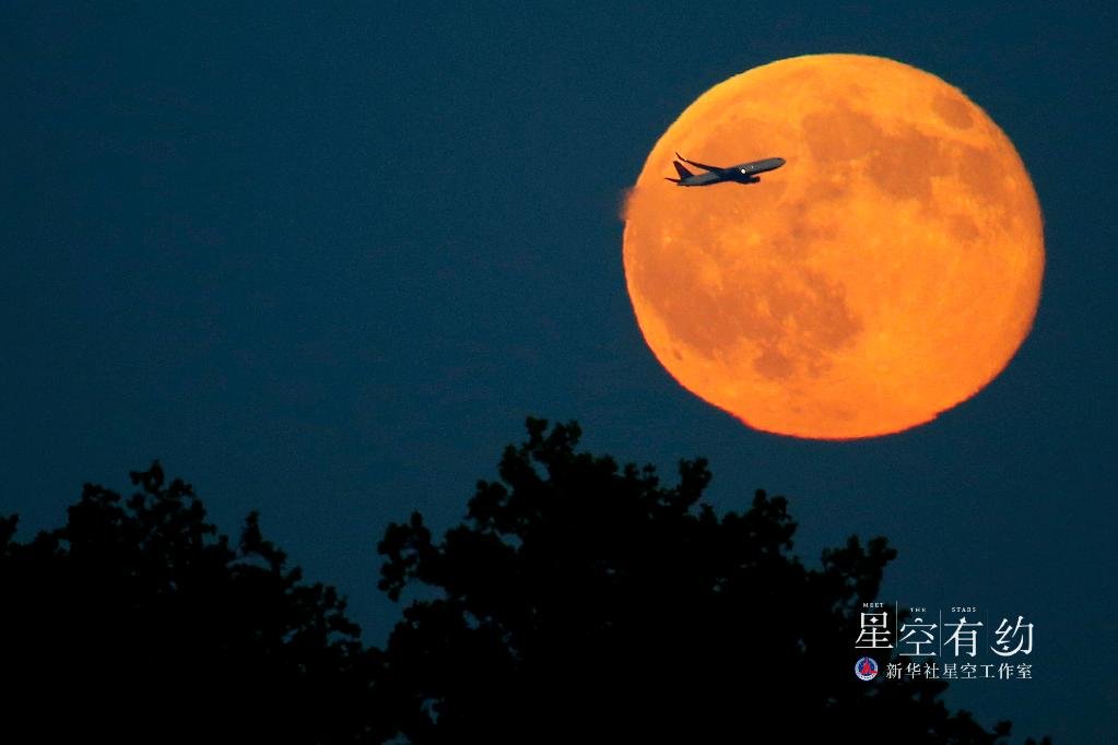 这是2015年7月31日在美国泽西城拍摄的一架飞机从“蓝月亮”前飞过。新华社/美联