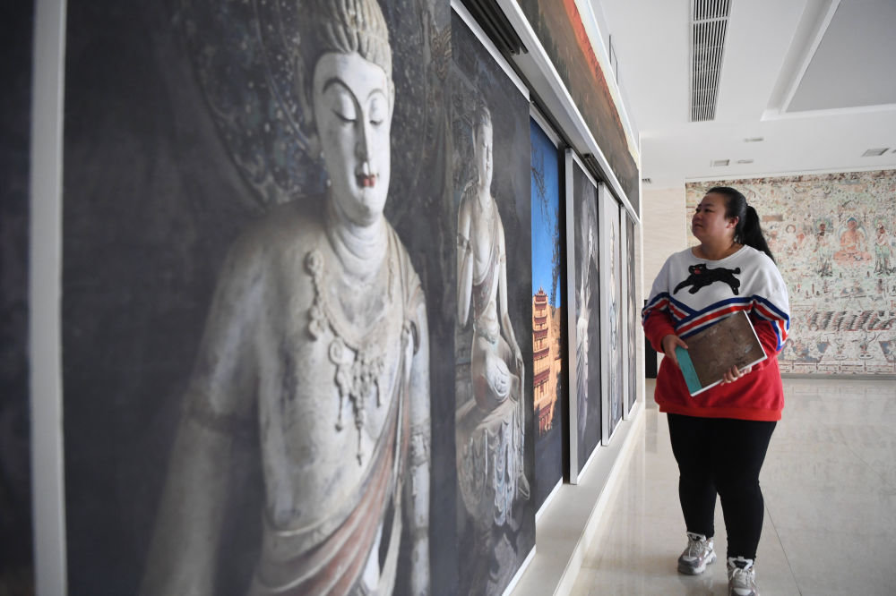 敦煌研究院文物数字化保护团队图像处理人员年海丽从莫高窟照片墙前走过（4月25日摄）。