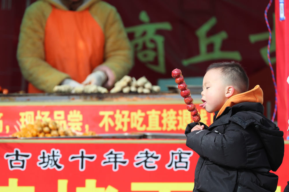 ↑1月25日，一名小朋友在河南省商丘市古城新年大集上品尝糖葫芦。新华社发（李恒 摄）