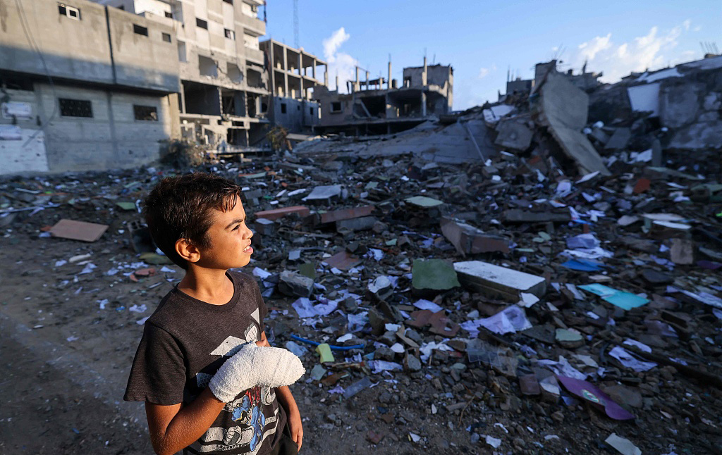 当地时间2023年10月16日，巴勒斯坦加沙地带，一名受伤的男孩看着被炸毁的家。