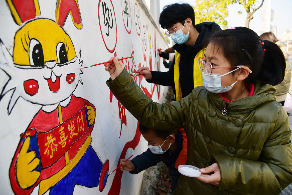 ↑ 1月11日，在江苏省镇江市远洋社区，江苏大学志愿者和小朋友一起描绘“年俗文化”主题墙画。新华社发（石玉成摄）