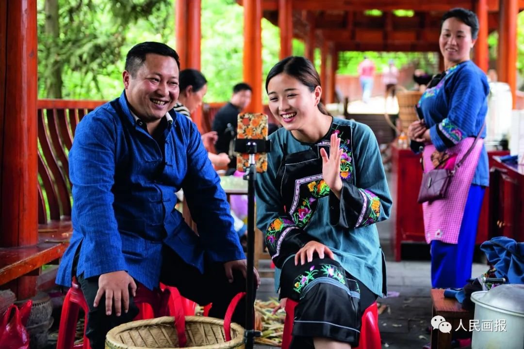 2020年5月15日,湖南湘西十八洞村扶贫队长麻辉煌(左)与返乡大学生施林娇(中)一起直播推销土特产。2021年,中国全面建成小康社会目标如期实现。摄影 陈思汗/新华社