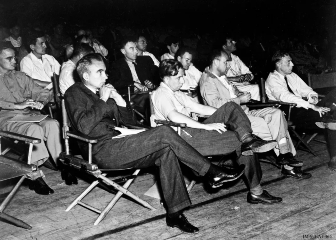 一群物理学家在1946年洛斯阿拉莫斯学术讨论会上。第二排左起第三位是奥本海默，他身穿黑色夹克，打着领带。图中出现的其他科学家包括恩里科·费米（Enrico Fermi）、爱德华·泰勒（Edward Teller）和理查德·费曼（Richard Feynman）。© Wikimedia Commons