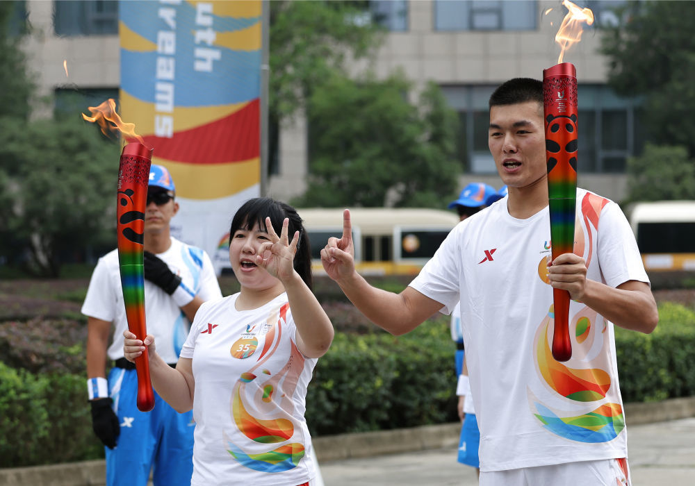 7月26日，大运会火炬手王政文（右）与陈丹在火炬传递中交接。新华社记者 骆学峰 摄