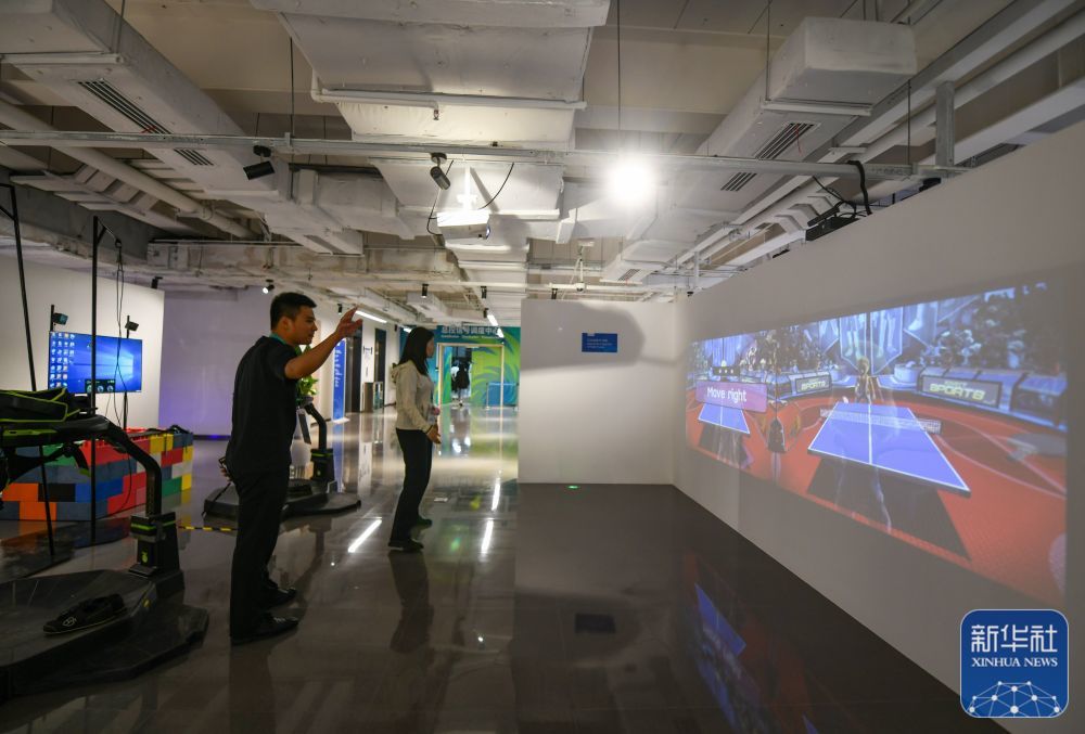 ↑ 7月13日,在成都大运会主媒体中心的休闲娱乐区,两名媒体记者在体验互动投影乒乓球。新华社记者 王曦 摄