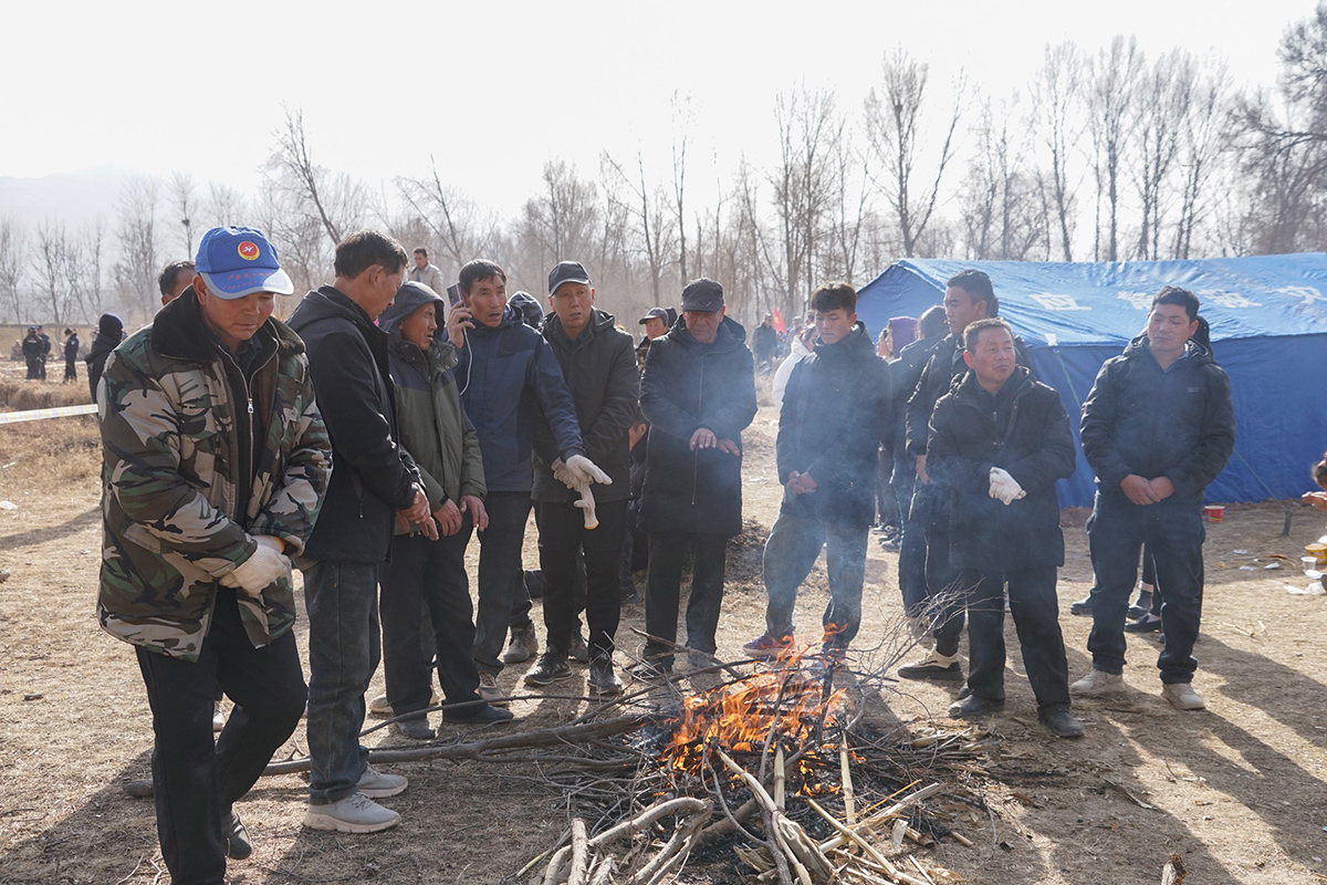 2023年12月19日，民众在救援现场外烤火取暖。中新社记者 马铭言 图