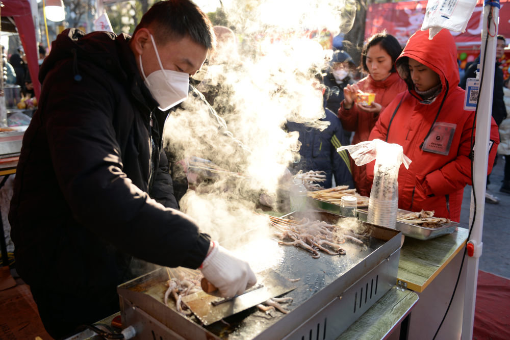 ↑1月24日，商贩在山东聊城古城区小吃一条街制作铁板鱿鱼。新华社发（孔晓政 摄）