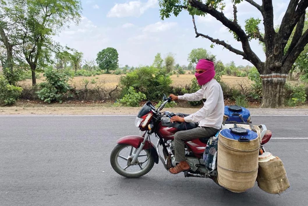 6 月 17 日，在印度北方邦勒利德布尔，一名送奶员在烈日下骑行，为防止牛奶在高温下变质，其搬运的奶罐均用湿麻袋包裹 新华社/美联
