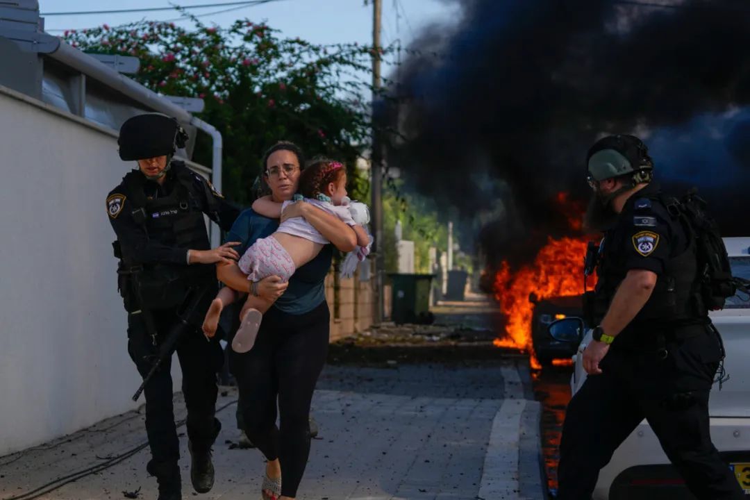 10月7日，在以色列南部的阿什凯伦，警察正在疏散一名妇女和一名儿童。（图源美联社）