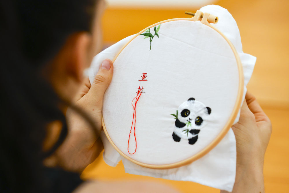 7月31日,成都大运村互动体验中心,阿根廷运动员亚拉·纳瓦罗体验在蜀绣作品上绣上自己的中文名字。新华社记者沈伯韩摄