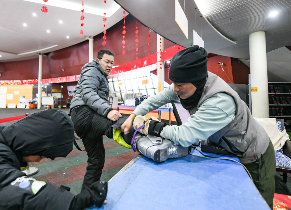 ↑2024年1月24日，罗甲久（右）在鹧鸪山滑雪场帮助游客脱雪鞋。新华社记者 王曦 摄