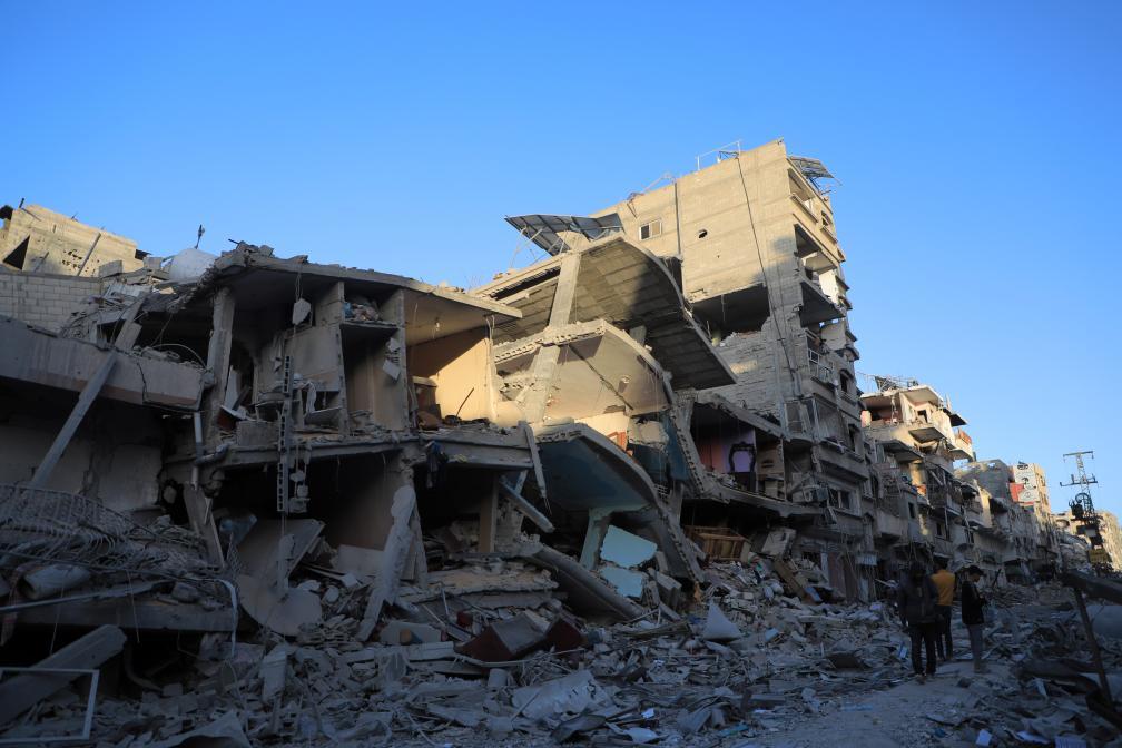 3月6日,在加沙地带南部城市汗尤尼斯,人们经过建筑废墟.