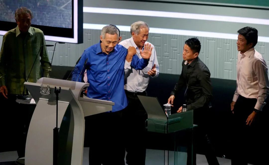 ·2016年8月21日，李显龙（着蓝衣者）在演讲时突感晕眩，国防部长黄永宏上前搀扶。