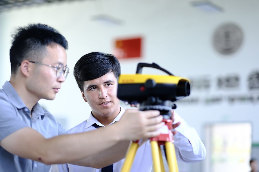 ↑6月14日，来自天津城市建设管理职业技术学院的老师（左）在塔吉克斯坦首都杜尚别的鲁班工坊内指导学生。