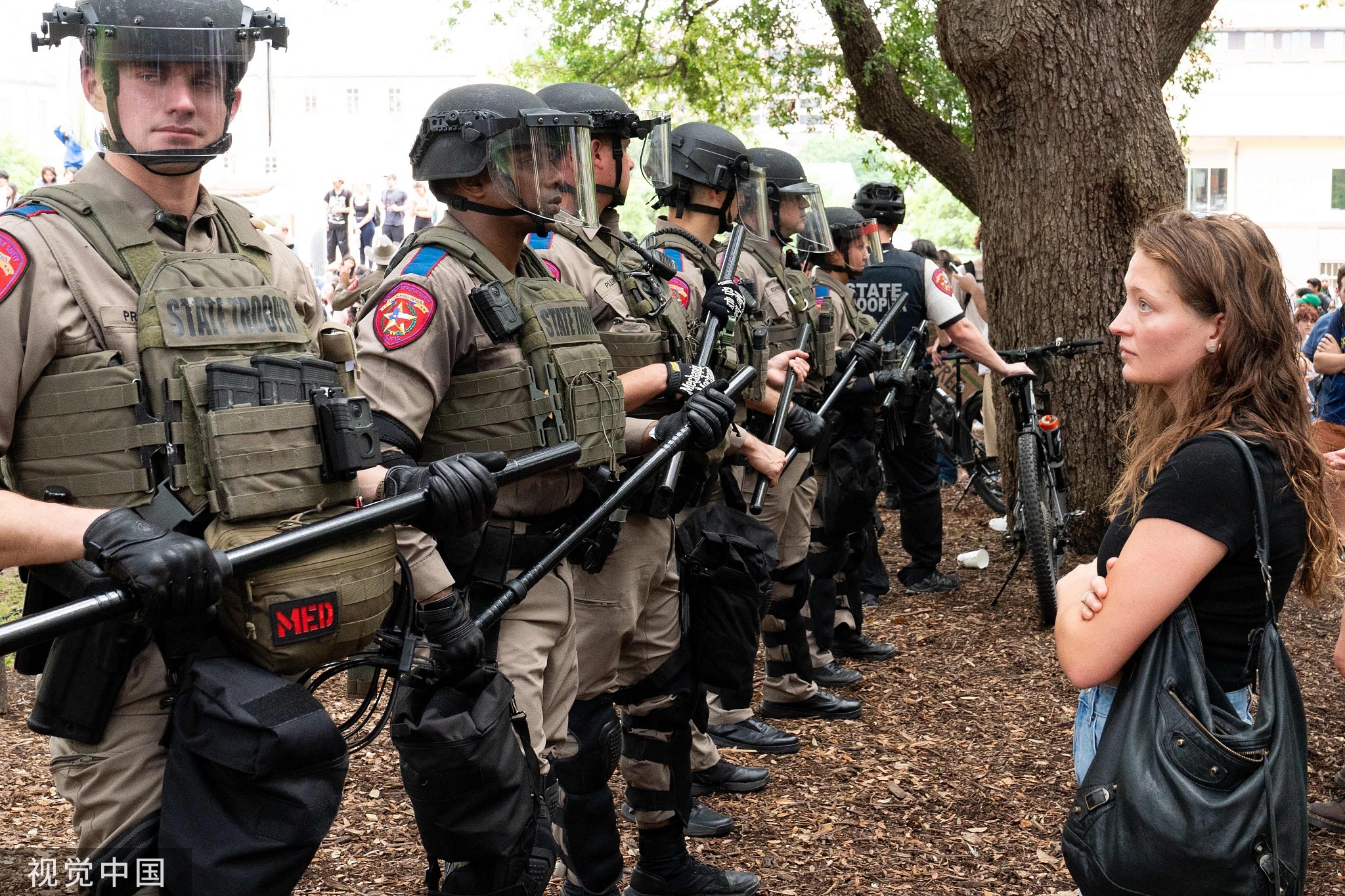 当地时间4月24日，得克萨斯大学校园内，一名抗议学生静静地盯着一排德州警察
