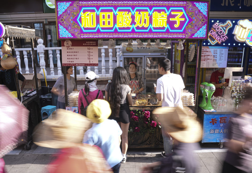 在位于乌鲁木齐市的大巴扎美食街，游客选购酸奶粽子。
