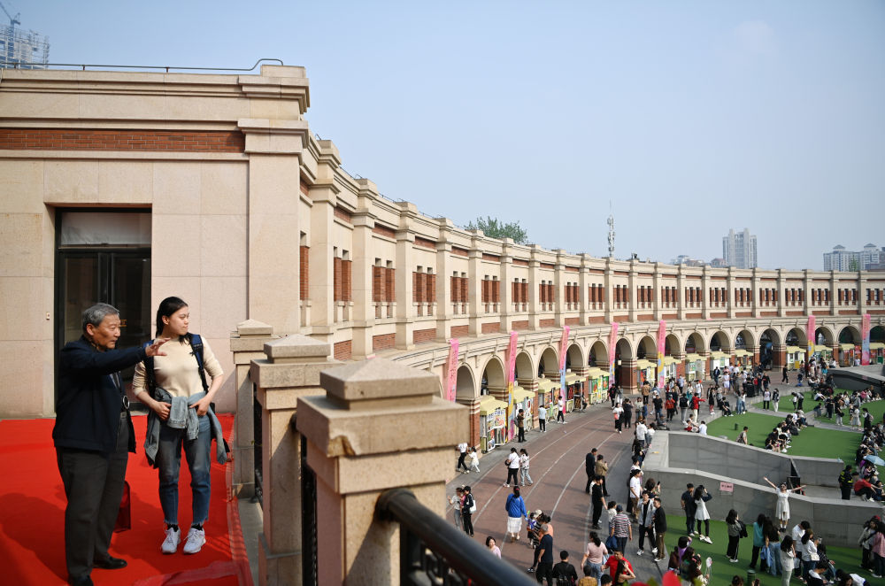 金彭育（左）向游客介绍五大道的民园广场（4月13日摄）。