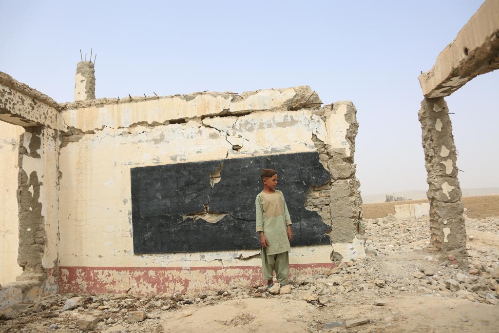 2022年8月23日，在阿富汗南部赫尔曼德省桑金地区，一名男孩站在废墟之中。桑金地区曾经最繁华的市场，如今遍布美军空袭留下的一个个巨大弹坑。新华社发（塞夫拉赫曼·萨菲摄）