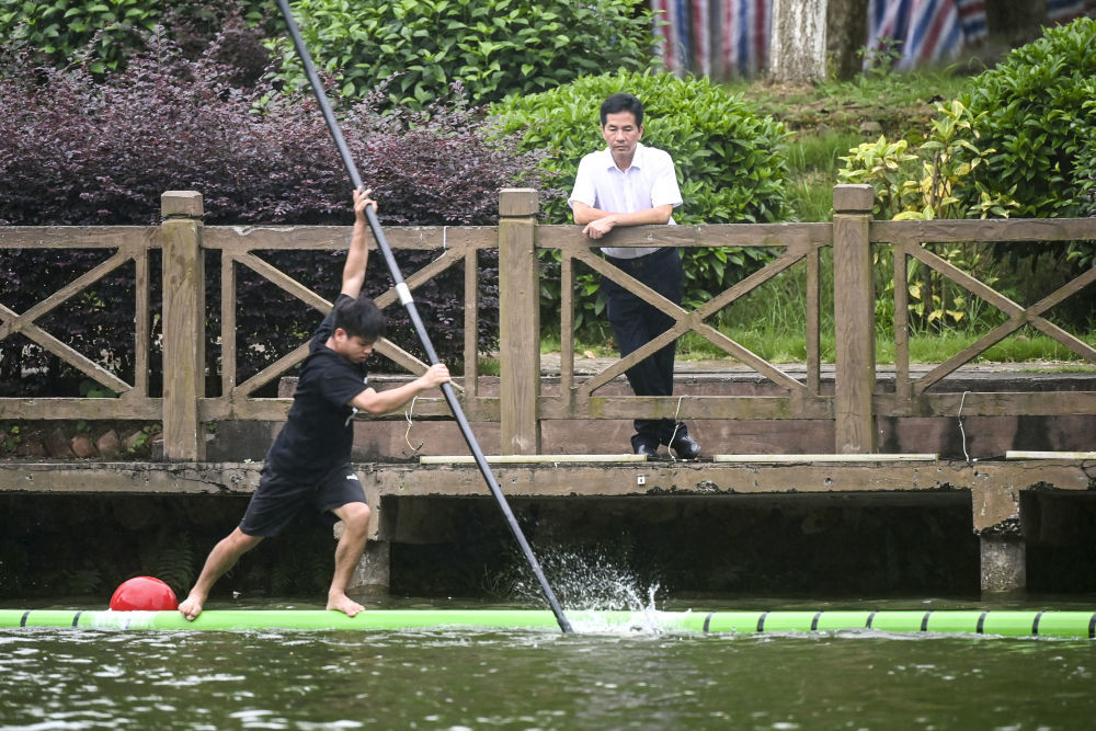 6月19日，蓝建卓（右）在观看独竹漂队队员的训练。