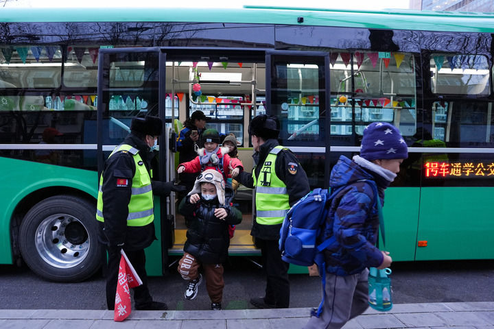 12月16日，北京公交集团通学368路车停靠在呼家楼中心小学通学车终点站，小学生在通学乘务员徐洁（后）和工作人员引导下下车。新华社记者 鞠焕宗 摄