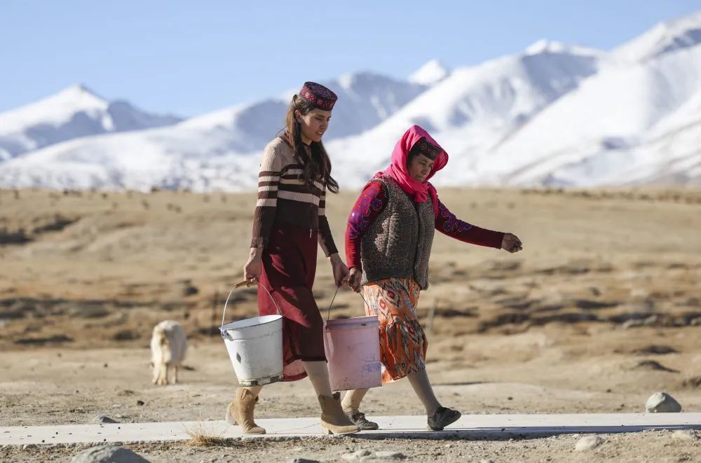 在新疆塔什库尔干塔吉克自治县瓦恰乡夏布孜喀拉村，艾尔开牙·多力开（左）帮母亲拎水。