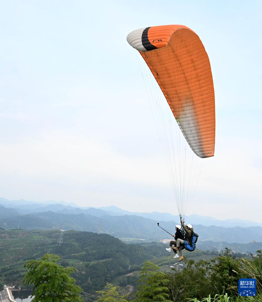 10月4日，游客在位于浙江省武义县的大斗山飞行营地体验滑翔伞，空中观赏茶园、花海风光。新华社发（张建成 摄）