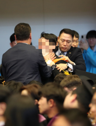 图为16日，在韩国科学技术院（KAIST）举行的学位授予仪式上，一名身穿黑色学士服的毕业生向尹锡悦喊话，却被韩国总统府警卫人员捂嘴强行退场 图源：韩媒