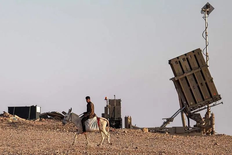 4月14日，以色列南部内盖夫沙漠一个未被以色列当局承认的村庄，一个男孩骑着驴靠近以色列铁穹导弹防御系统的电池。图源：视觉中国