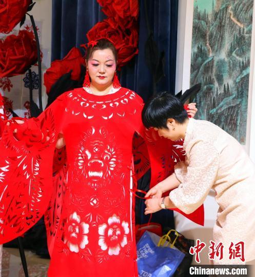 扎伊诺&middot;毛尼亚孜在工作人员的帮助下穿戴“龙凤呈祥”剪纸时装。韩欢欢 摄