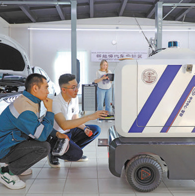在哈萨克斯坦鲁班工坊新能源汽车实训区，两名技术员正在操作调试智能机器人车。本报记者 赵益普摄