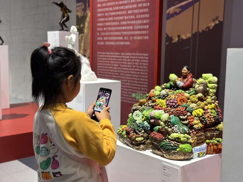 6月25日，在内蒙古自治区呼和浩特雕塑艺术馆，一名小朋友正在用手机记录象征丰收的雕塑作品。中青报·中青网记者 石佳/摄