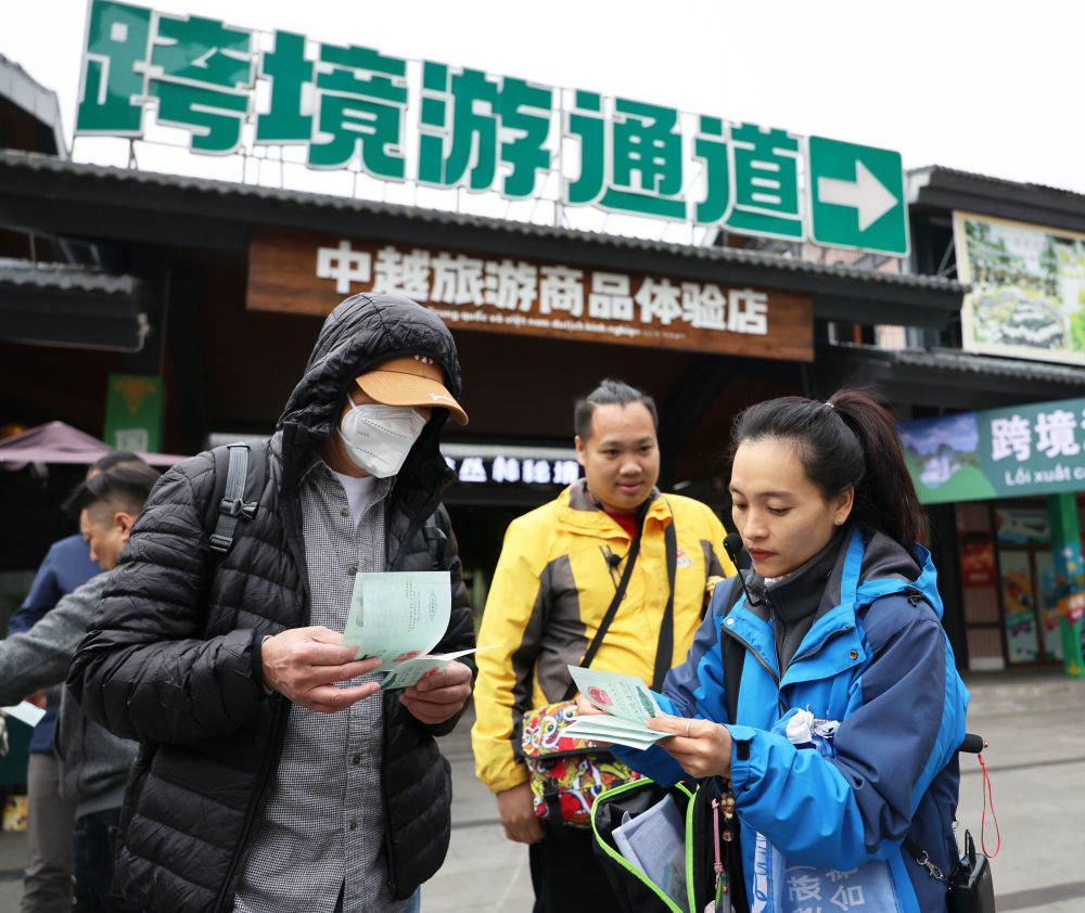 12月15日，在中越德天（板约）瀑布跨境旅游合作区，成团导游（右）向游客分发跨境游出入境通行证。